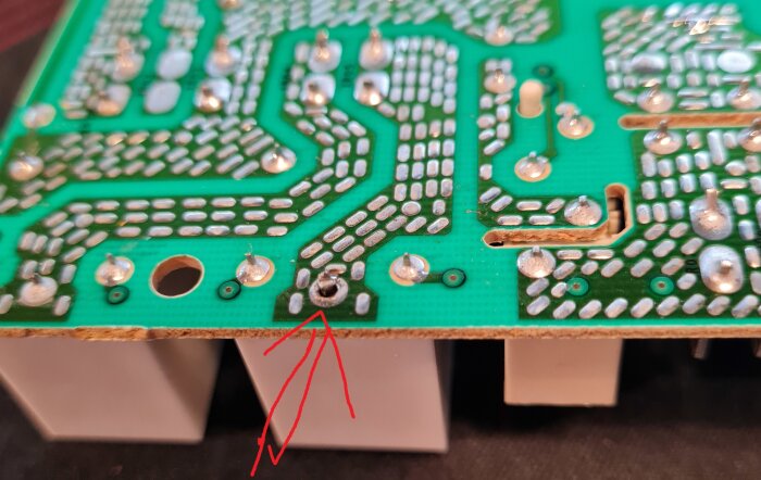 Undersidan av ett kretskort med en dålig lödning markerad med en röd pil. Kretsen ser annars hel ut.