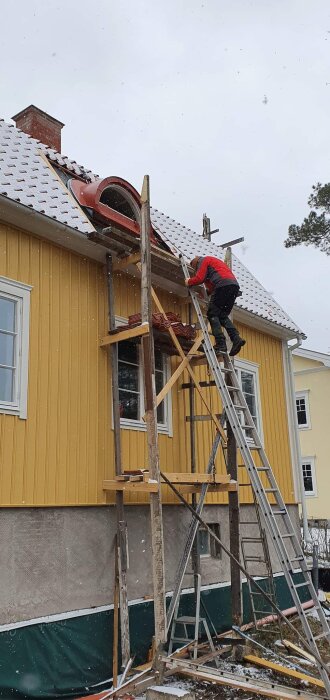 Person på stege installerar takfönster på ett gult hus under vintriga förhållanden.