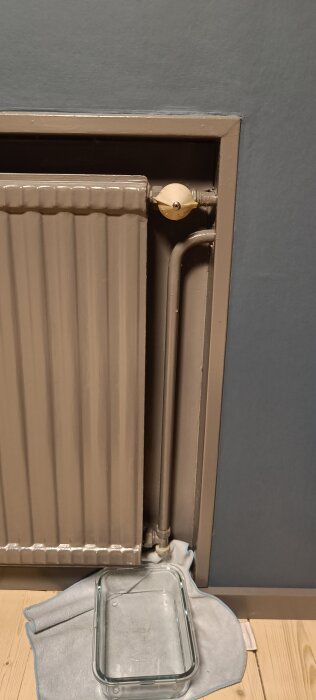 Radiator i källare med gammal ventil som läcker, burk på golvet för att fånga upp vatten.