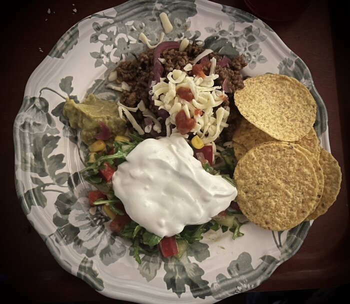 Tallrik med tacorester, inklusive köttfärs, grönsaker, ost, guacamole, gräddfil och nachochips.