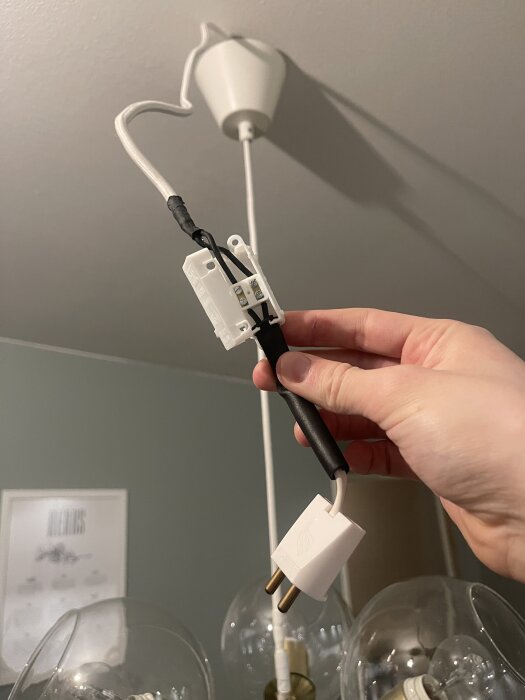 Närbild av en hand som håller i en lampsladd med stickpropp och sockerbit mot taket med en takkontakt i bakgrunden.