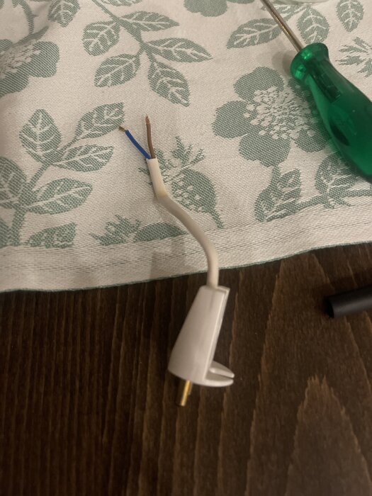 Kabel med två exponerade ledningar på en blommig duk, tillsammans med en grön skruvmejsel.