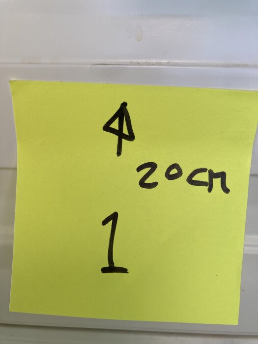 Gul post-it med siffran "1", en pil och texten "20 cm" fäst på en vit kökslucka.