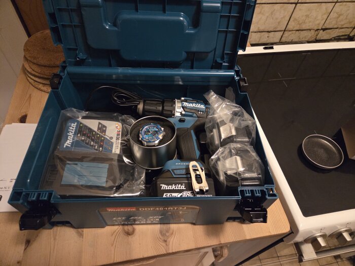 En öppen Makita-verktygslåda på ett bord, innehållande en borrmaskin, batterier och en ny klocka i blått.