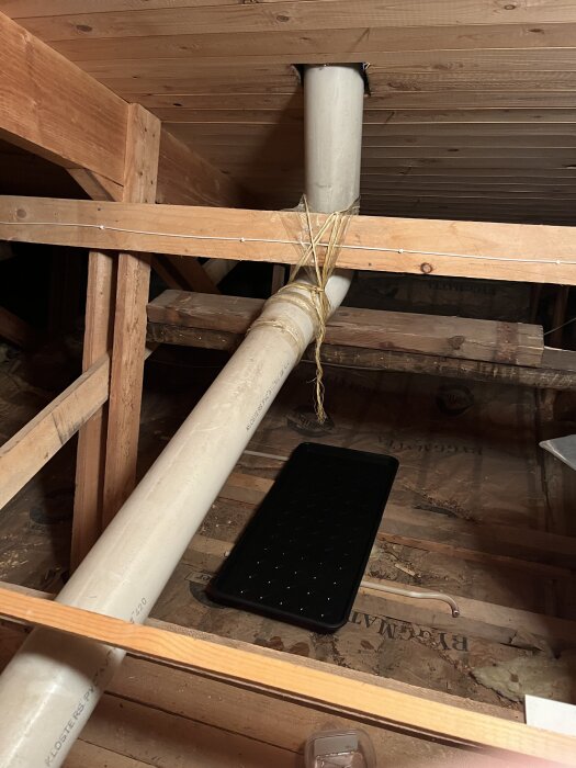 Rör genom taket på vinden med uppsamlingskärl under, fäst med snöre; används för att hantera kondens eller eventuellt läckage ovanifrån.