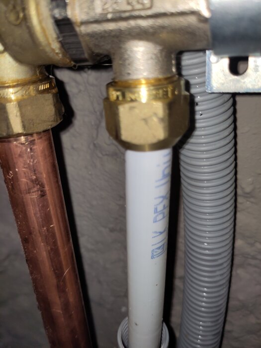 Närbild på VVS-installation med kopparrör, vitt plaströr och grå kabelslang, anslutna med mässingskopplingar.