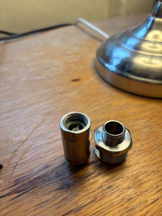 Två metallnipplar placerade på ett träbord, varav den högra har grövre gängor.