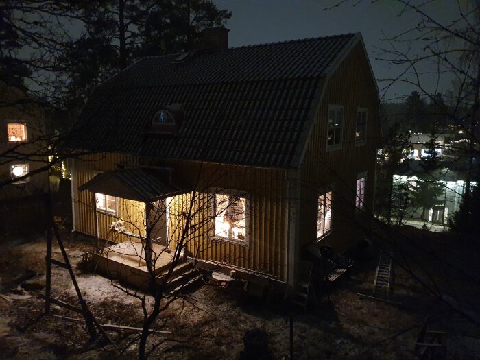 Hus med nytt takfönster, sett på natten med upplyst veranda och omgivande träd. Nyutvecklat projekt nära bygglovstidens slut.