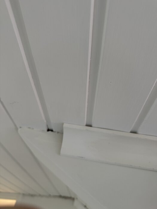 Närbild på taklistens avslut i hörn med vitmålat träpaneltak.