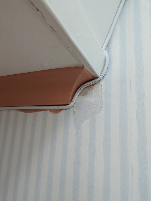 En närbild på en vägg med en kabel som följer trappkanten. En del av listen är installerad och väggytan bakom visar tecken på renovering.