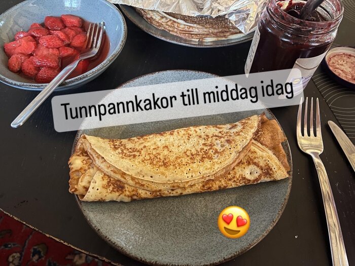 Tunnpannkakor serverade på en tallrik med en skål jordgubbar och syltburk bredvid, text "Tunnpannkakor till middag idag" över bilden.