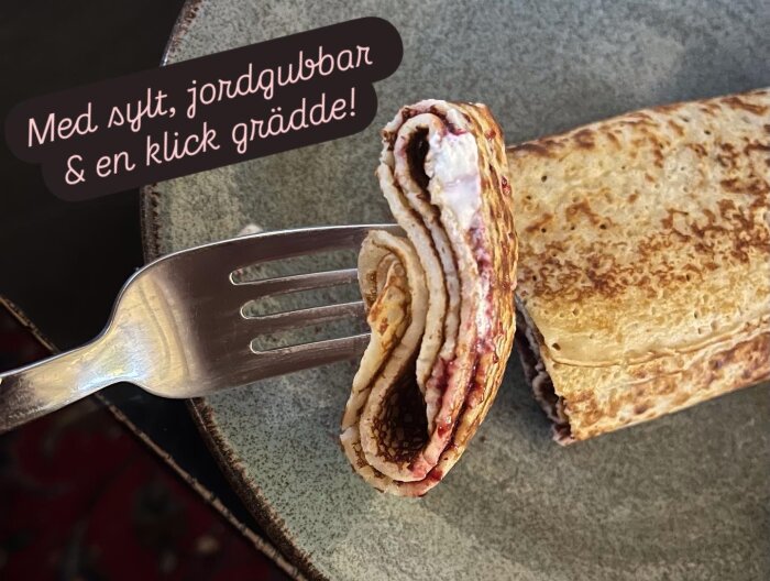 Pannkakor på en tallrik med en gaffel, fyllda med sylt, jordgubbar och grädde.