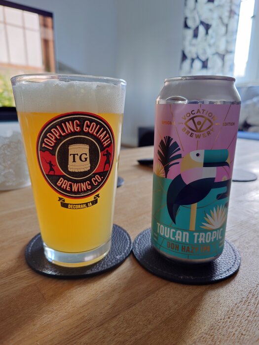 Ett glas öl från Toppling Goliath Brewing Co. och en burk Vocation Brewery's Toucan Tropic DDH Hazy IPA på ett bord.