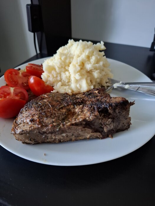 Tallrik med grillad fläskkarré, potatismos och körsbärstomater.