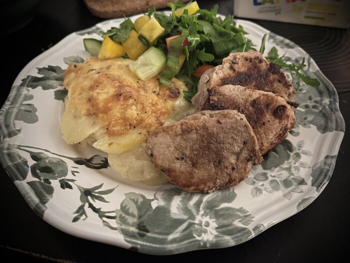 Stekt fläskfilé, potatisgratäng och sallad på en blommig tallrik.
