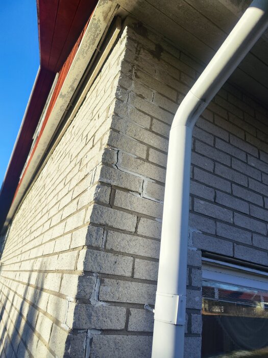 Sprucken fasad med tegelstenar och stuprör vid en husvägg.