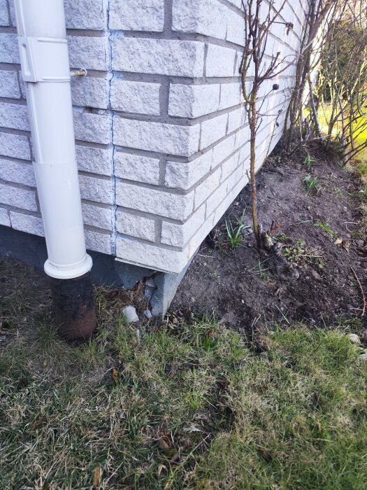 Skadat hörn av tegelvägg med sprickor, intill stuprör och gräsyta.