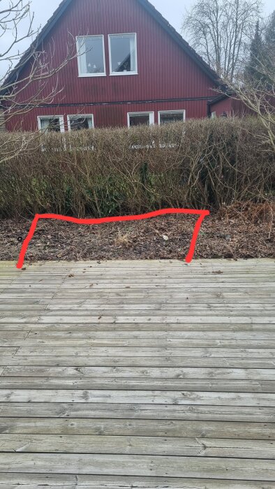 Trädäck vid en röd byggnad, med ett markerat område på marken där däcket planeras att byggas ut.