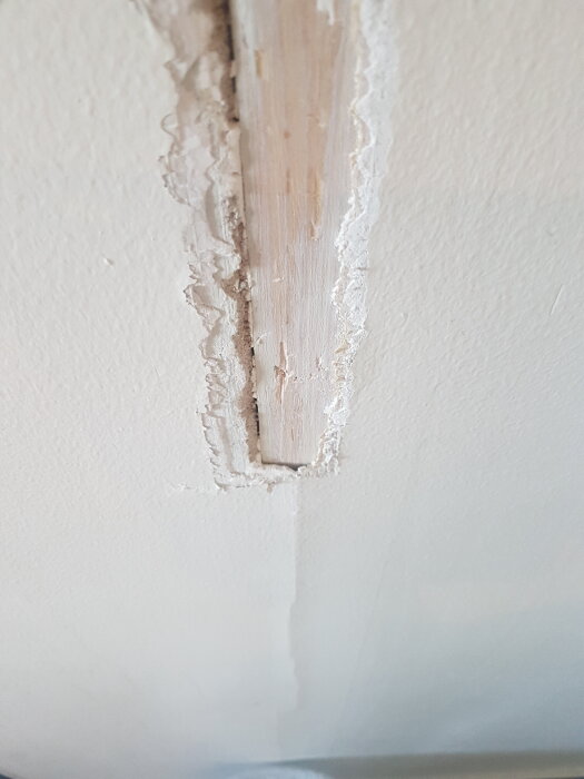 Sprucket spackel runt en gammal dörröppning, där spacklet har släppt och en träbit är synlig.
