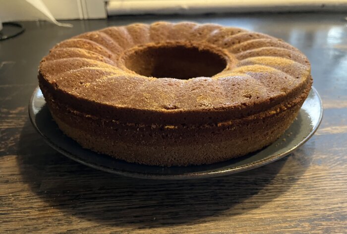 Pepparkakssockerkaka med mandelmjöl på ett fat, rund form med marmorerad yta, synlig luftighet och ojämn missfärgning av ströbröd.