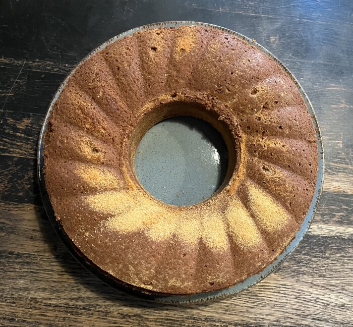 Rund brun sockerkaka på ett fat, med ojämn spridning av ströbröd på toppen och lite missfärgning, bakad med mandel- och vetemjöl.