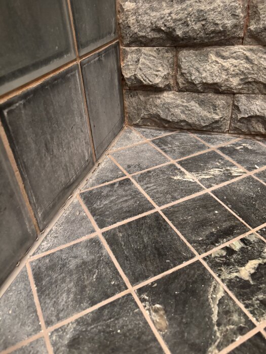 Matt och repigt badrumsgolv i grön natursten med missfärgning, bredvid strukturerad vägg.