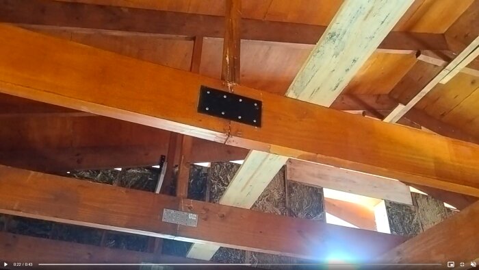 Wooden ceiling structure with visible beams and metal connector plates, highlighting structural concerns for building reinforcement.
