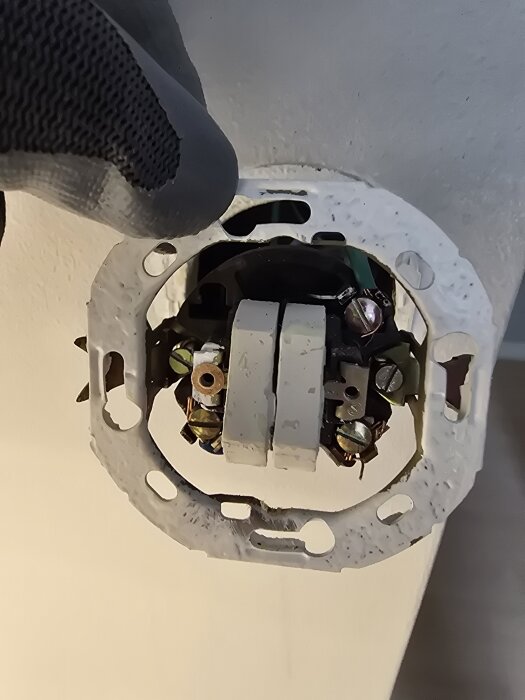 Elektrisk brytare delvis bortmonterad med kablar och en hand i arbetshandske som håller den.