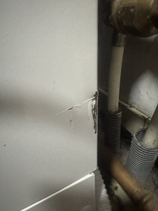 Närbild av ett skadat område på sidan av en installation, med repor och märken, omgiven av rör och kopplingar.