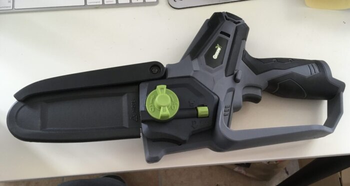 Batteridriven motorsåg från Meec Tools, liggande på ett bord. Svart och grå design med gröna justeringsknappar.