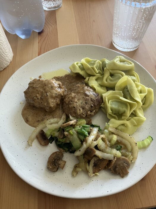Biffar i pepparsås, spenat- och ricottapastakuddar samt fräst pak choi och svamp på en tallrik på ett bord.