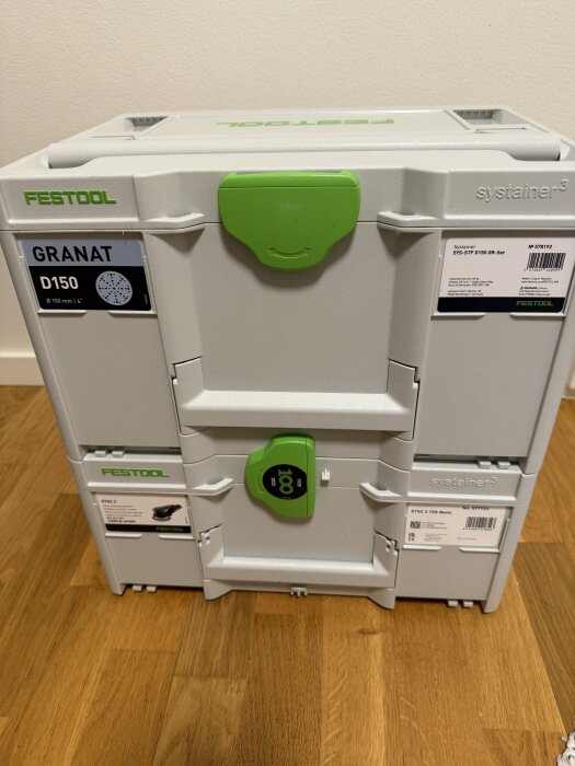 Verktygslåda Festool Systainer med gröna handtag och etiketter; står på ett trägolv.