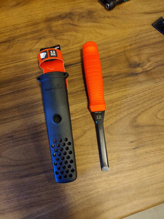 Stämjärn med orange handtag och svart skydd, 12 mm bredd, ligger på ett träbord.