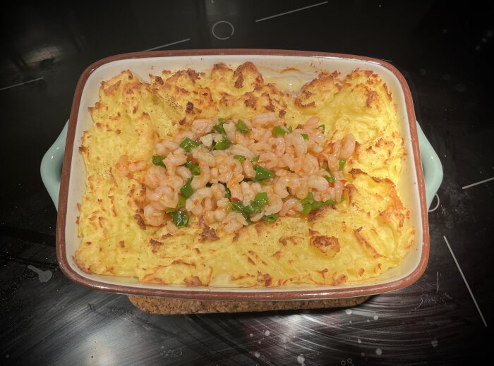 Hemlagad fiskgratäng med potatismos, salladslök, padrones, torsk och stekta räkor i sweet chilisås i en ugnsform.