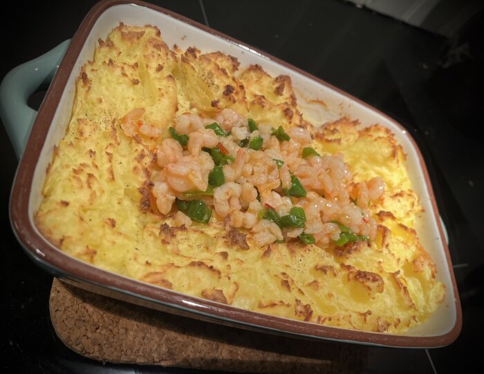 Hemlagad fiskgratäng med potatismos, salladslök, padrones, torsk, och stekta räkor i sweet chilisås i en ugnsform.