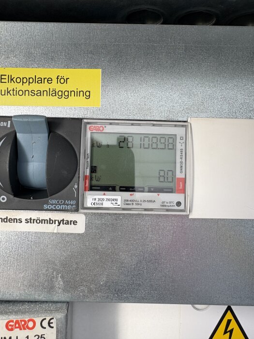Elskåp med en mätare från Garo som visar energiförbrukning i kWh och aktuellt värde på 8.0, intill en huvudströmbrytare.