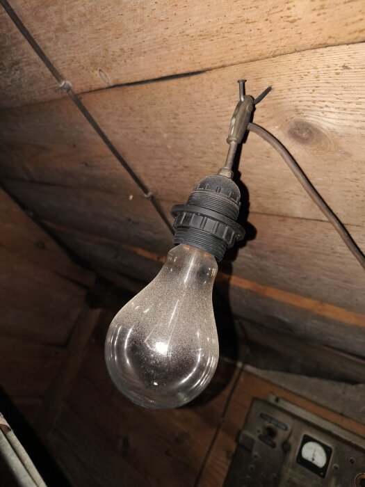 Gammal glödlampa hänger från ett trätak, del av en diskussion om lampor och antikviteter.