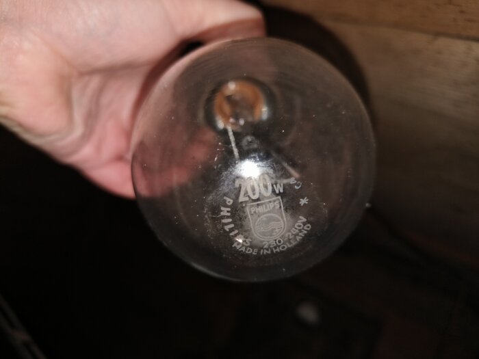 Gammal Philips 200 W glödlampa i en hand, text på glödlampan synlig.