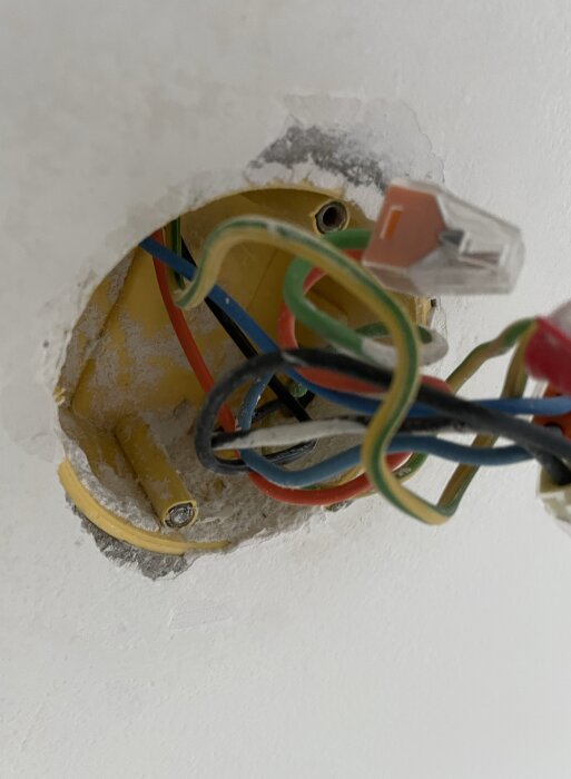 Kablar och en takdosa med en avbruten skruv i ett gult plastfäste i taket.