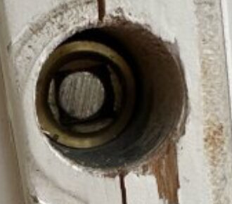 Ett närbildsfoto på en trähålighet med en lös, snurrande del inuti, omgiven av slitna kanter och ovanligt placerade skruvar.