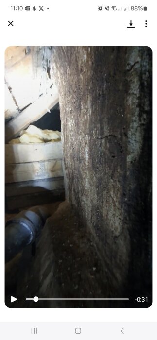 Missfärgad murstock på vinden med tecken på eventuell läckage eller djurspillning vid foten.