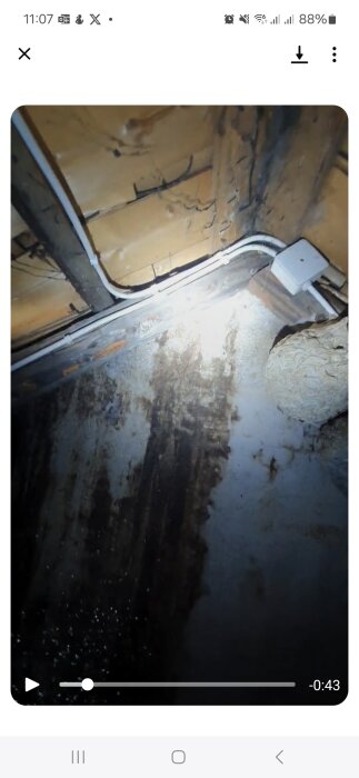 Missfärgad murstock på vinden med mörka ränder som ser ut som om något runnit. Det finns ledningar och något som liknar musbajs nära foten.