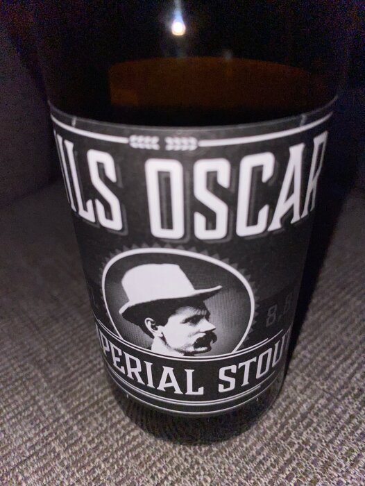 Flaska med etikett "Nils Oscar Imperial Stout", svartvitt porträtt, text "Imperial Stout" synlig.