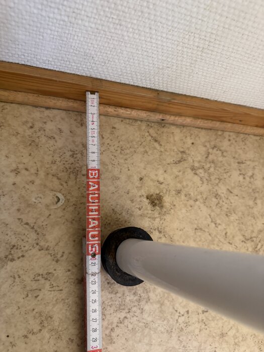 Mätbild av avloppsröret på en gästtoalett, med ett måttband som visar avståndet från väggen till röret på cirka 22 cm.