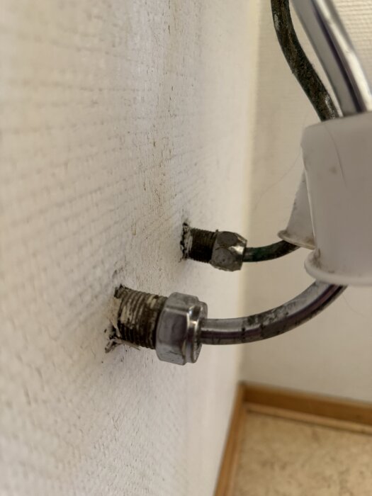 Korrodade vattenrör och kopplingar på vägg, del av renoveringsdiskussion kring en gästtoalett i ett äldre hus.