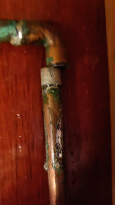 Kopparrör med korrosion och isärfruset böjstycke i ett stall, nära trävägg. Letar efter lösning utan rörmokare eller lödning.