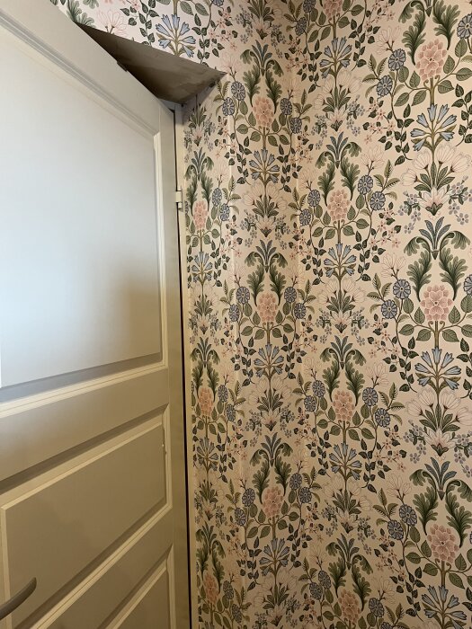 Blommig tapet med mönster runt dörr och snedtak i rum, med detaljerad bladmönstring.