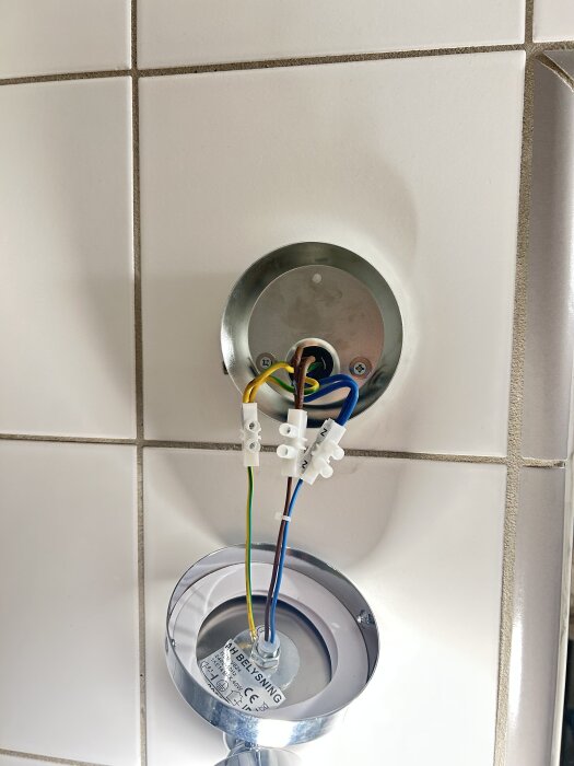 Anslutna elledningar i en lampa mot kaklad vägg.