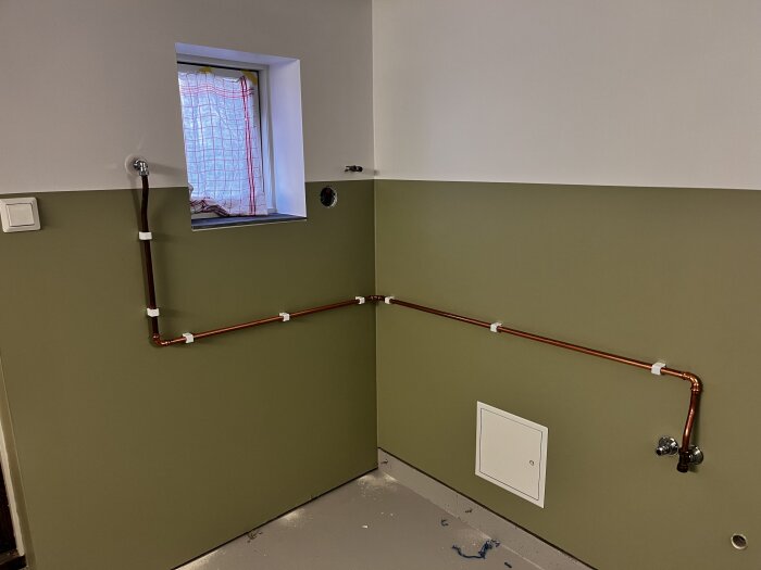 Väggmonterade kopparrör monterade för vattenutkastare, Vit vägg med grön panel, kopparrör och fästen vid ett fönster.