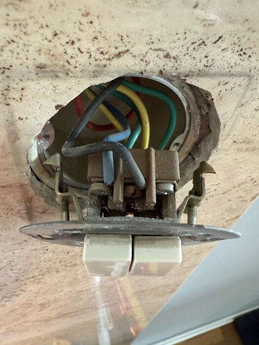 Gammal elektrisk brytare med flera färgade ledningar, monterad i en vägg eller tak, använd för att styra belysning.